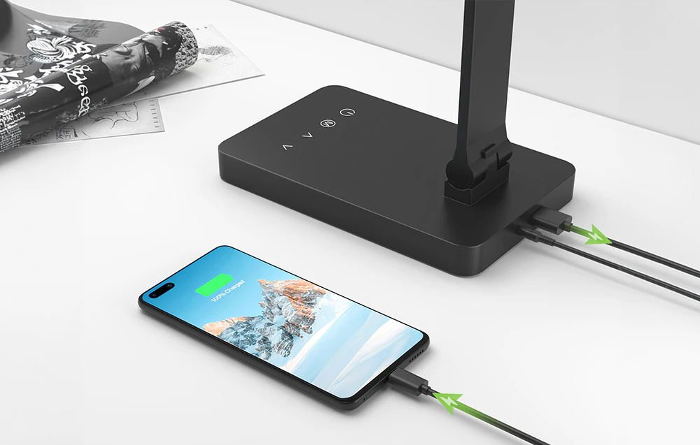 Un smartphone conectat la o lampă neagră pe o masă albă pentru a se încărca