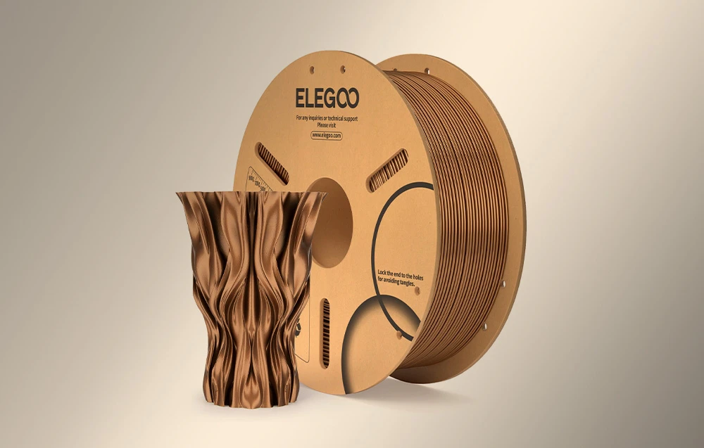 Bobină de filament 3D ELEGOO în culoarea aramă lângă o vază elegantă cu o suprafață ondulată, în spirală, imprimată în aceeași nuanță