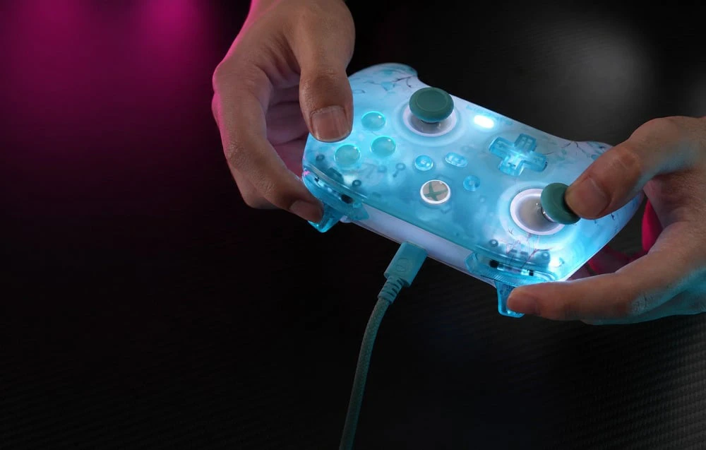 Mâini ținând un controler de jocuri cu iluminare din spate și un cablu USB pe un fundal întunecat