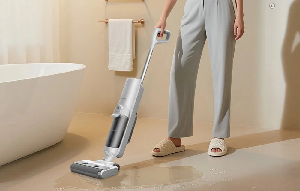 O femeie îmbrăcată în pantaloni gri folosește un aspirator vertical Proscenic pentru a curăța apa vărsată de pe gresia unei băi moderne
