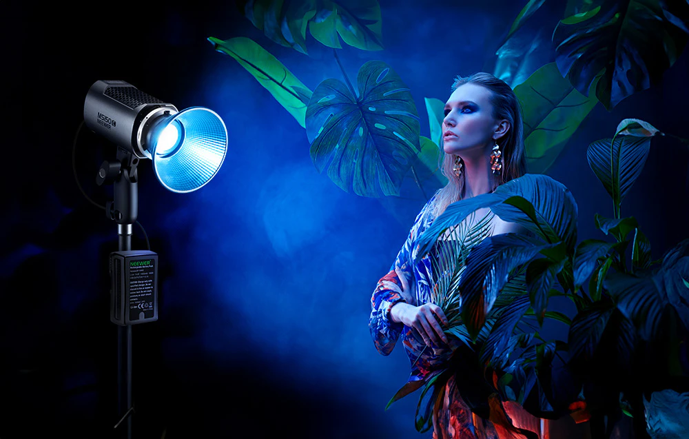 Sesiune foto cu lampă Neewer ce emite lumină albastră și model în ținută colorată printre plante