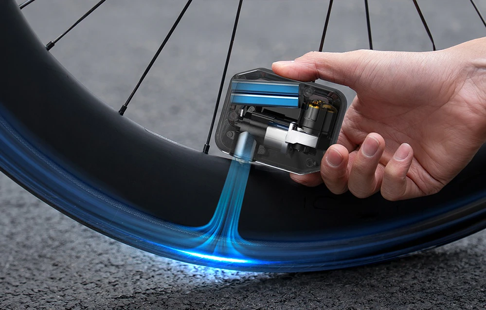 O mână care ține mini-pompa electrică AS280PRO lângă o roată de bicicletă în timp ce umflă o anvelopă