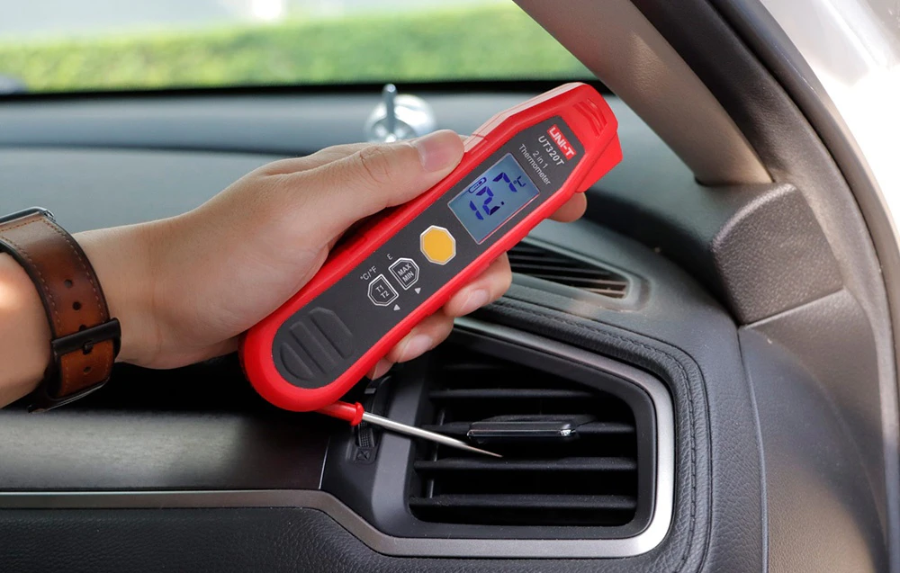 Mână ținând un termometru electronic cu sondă, măsurând temperatura lângă o gură de aerisire a mașinii