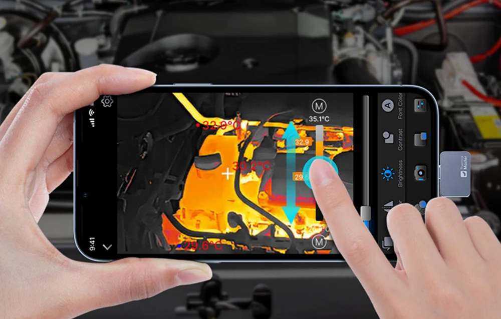 Un deget indică punctele fierbinți de pe motorul unei mașini, capturate de o mini-cameră de termoviziune pe ecranul smartphone-ului