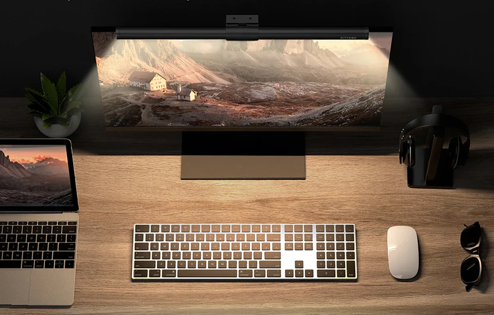 Birou cu un laptop, tastatură, mouse și monitor cu o lampă montată pe acesta, privit de sus