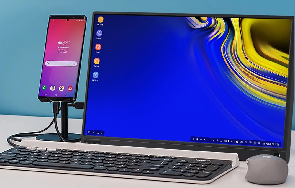 Monitor portabil în modul Samsung DeX conectat la un smartphone pe un trepied, cu o tastatură și un mouse Logitech în apropiere