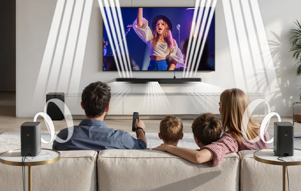 O familie care urmărește un concert la televizor într-o sufragerie cu două difuzoare, un subwoofer și o bară de sunet