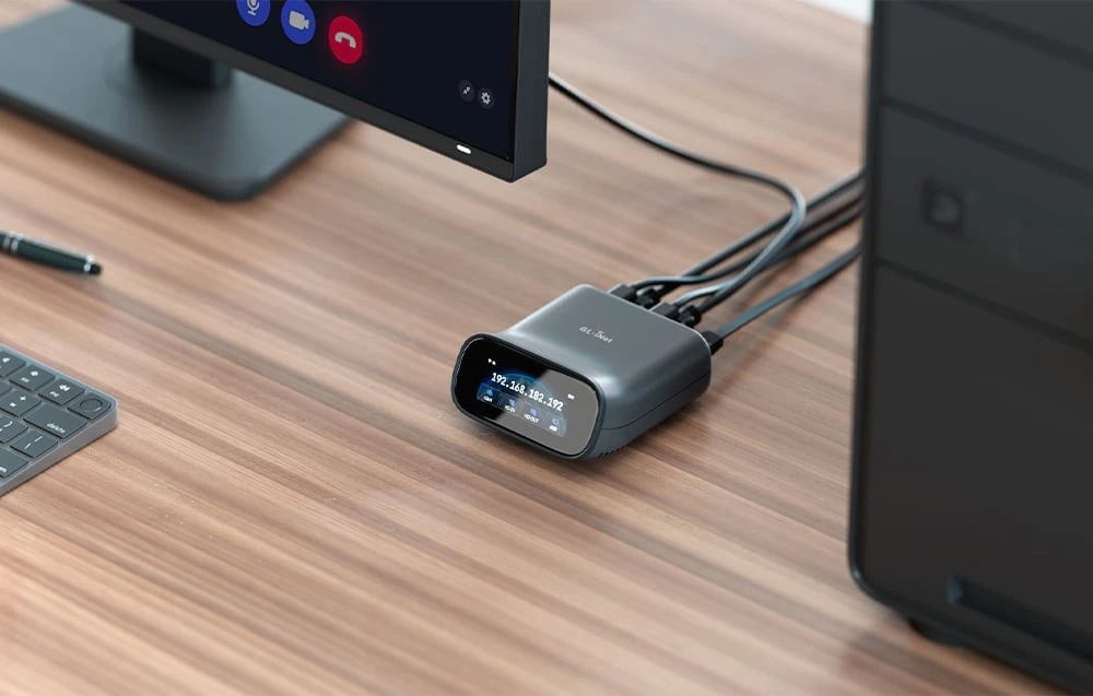 Un comutator KVM conectat prin cabluri pe un birou; lângă acesta se află un computer de birou și un monitor cu un sistem de videoconferință