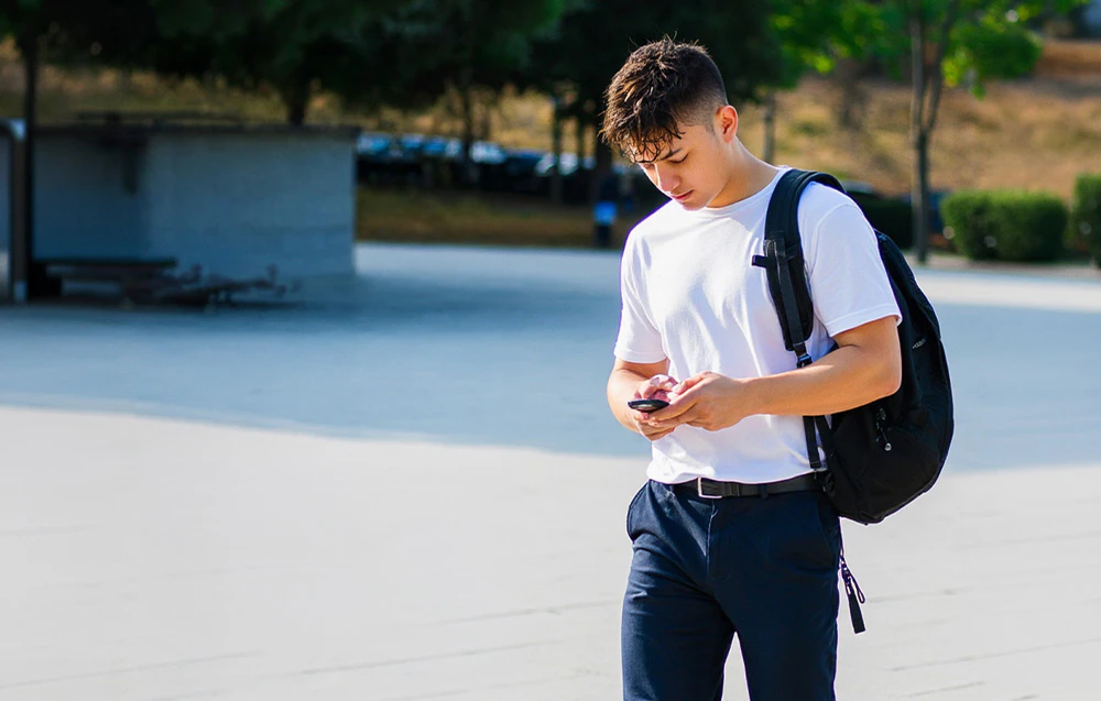 Un tânăr cu un rucsac și un smartphone în mână