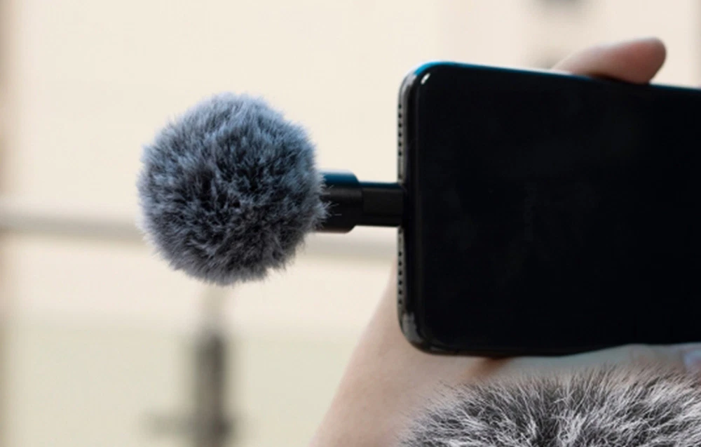 Smartphone ținut în mână cu un microfon mic atașat, prevăzut cu un paravan din blană