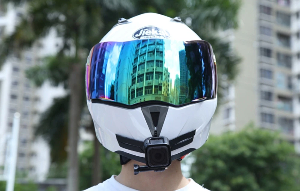 Cască albă de motocicletă cu vizieră colorată și o cameră de acțiune mică montată pe bărbie, vedere din față.
