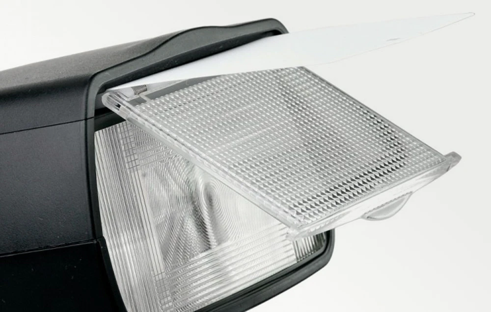 Prim-plan al capului blițului negru cu difuzorul transparent extins și o placă reflectorizantă albă