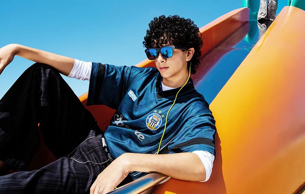 O persoană care poartă ochelari de soare cu lentile albastre și un tricou sport albastru stă pe un tobogan portocaliu
