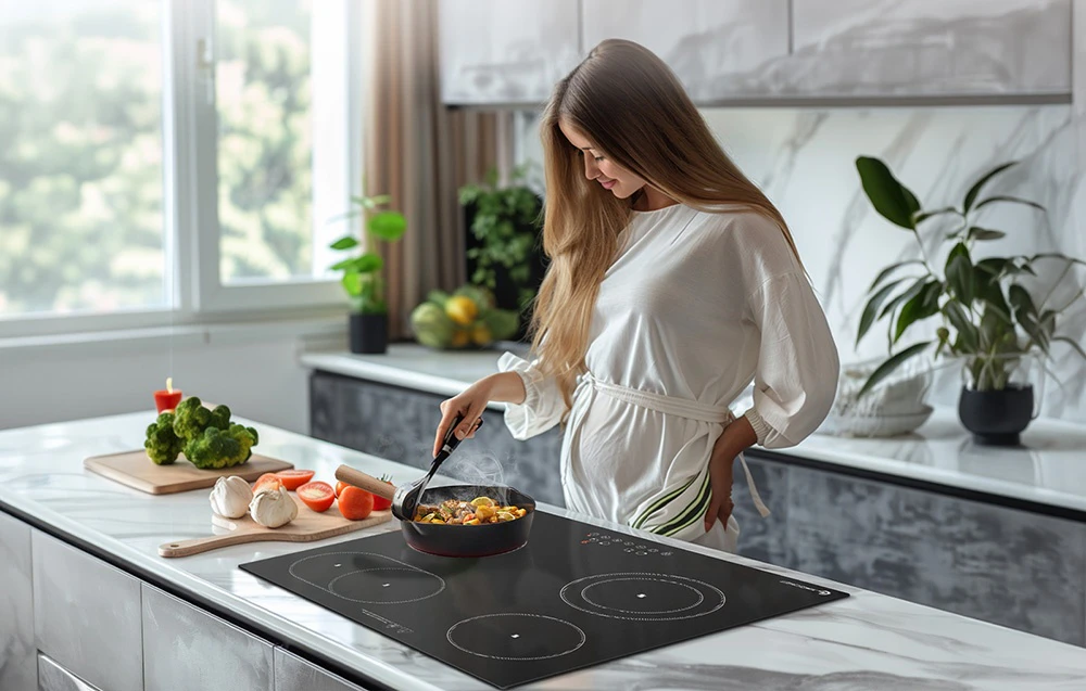 O femeie prăjește legume într-un wok pe o plită ceramică AMZCHEF neagră, încorporată într-un blat de marmură de culoare deschisă