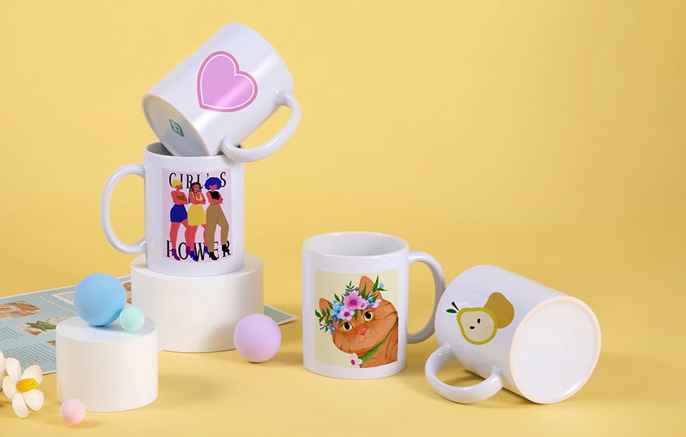 Două stive de căni de ceramică cu diverse imprimeuri stau pe piedestale albe.
