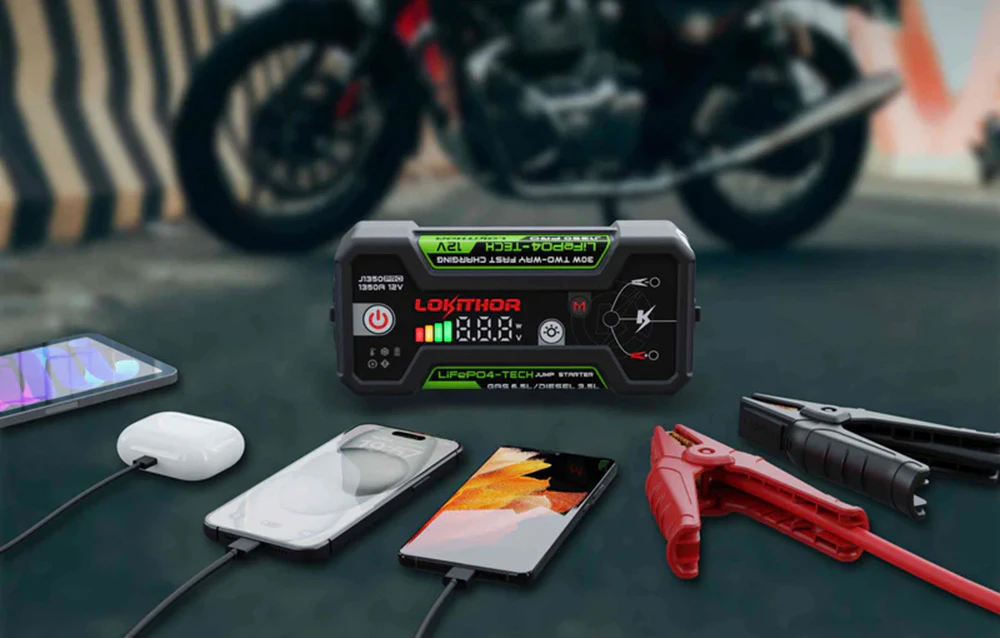 Dispozitivul de pornire LOKITHOR pe asfalt, încărcând smartphone-uri și căști lângă o motocicletă.