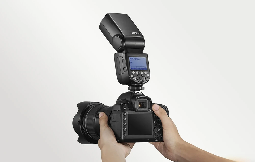 Aparat foto cu blițul Godox V860III ținut în mâini, prezentând ecranul LCD iluminat din spate