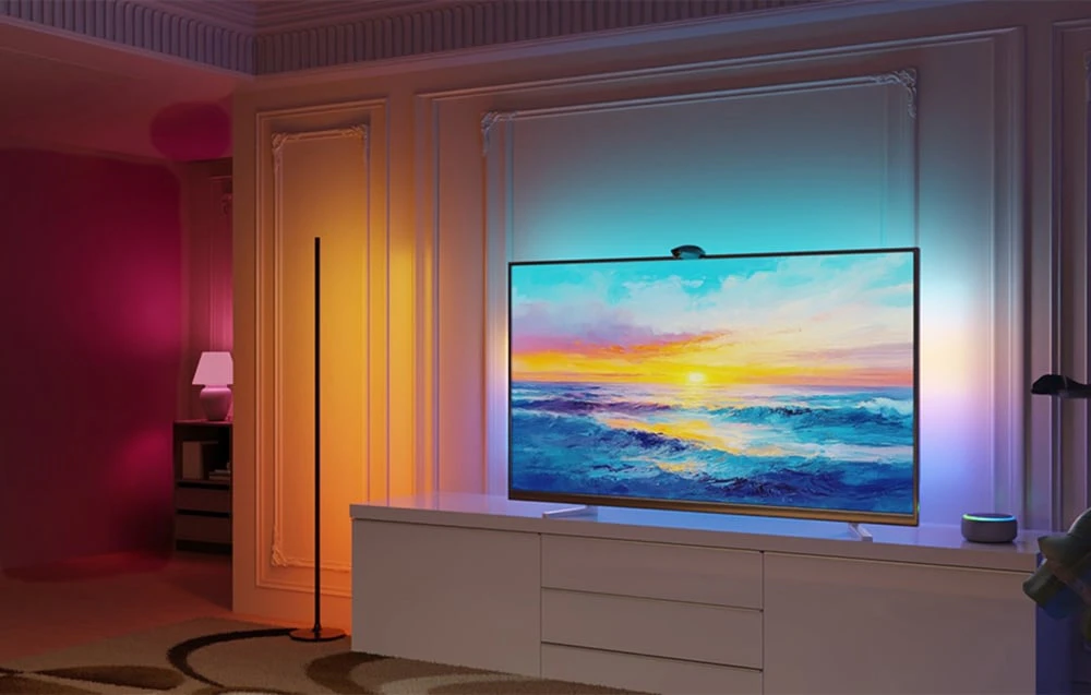 Camera de zi cu o comodă, un televizor și o lampă de podea care proiectează lumină colorată în cameră