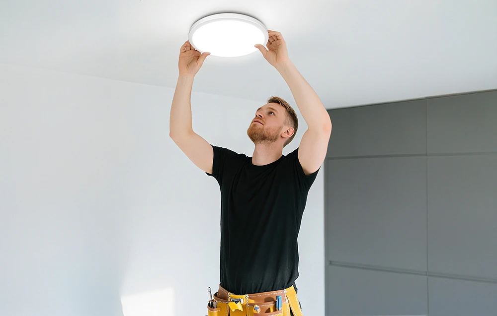 Un bărbat instalează un plafonier într-o cameră luminoasă