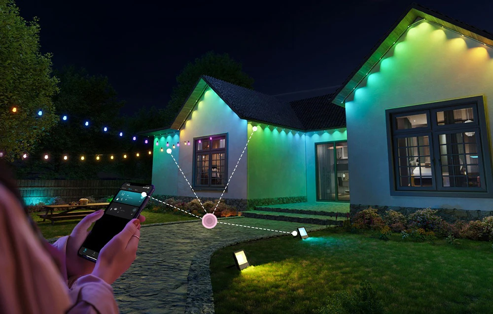 Casă iluminată de lumini colorate; în stânga, o femeie ținând un smartphone