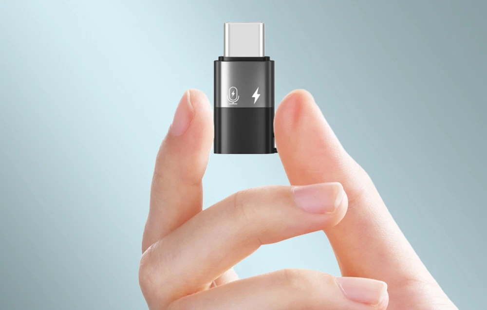 Imagine mărită a unui adaptor USB-C mic ținut între degete, pe un fundal albastru deschis.