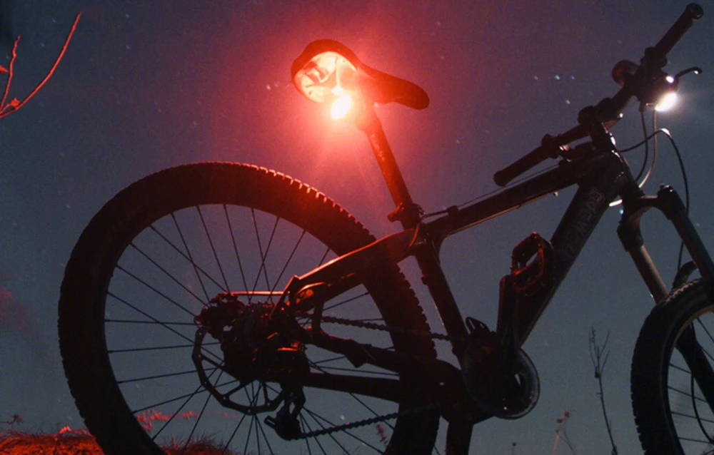 Bicicletă de munte cu lumina roșie din spate aprinsă pe cerul de seară cu stele