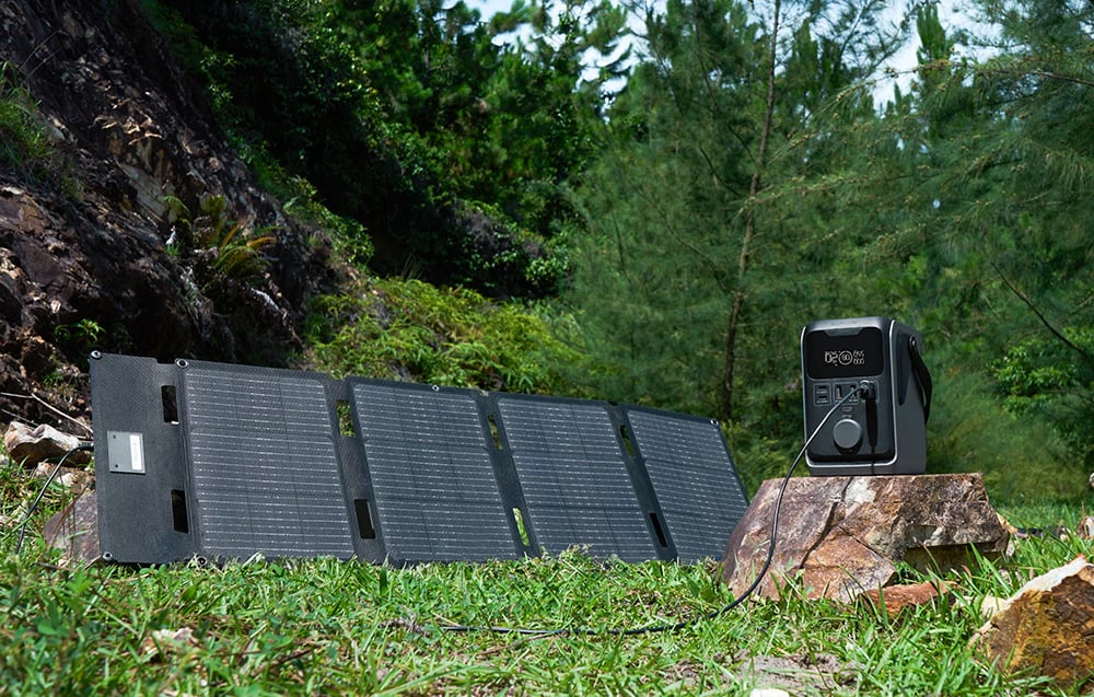 Un panou fotovoltaic conectat la o stație electrică portabilă care stă pe o stâncă în pădure