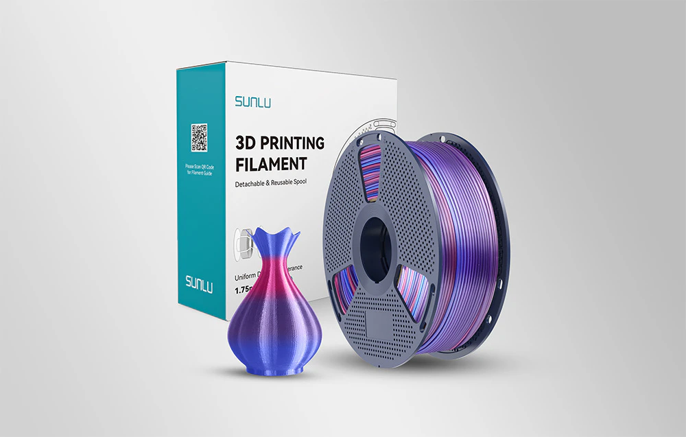 O bobină de filament violet-albastru lângă o cutie albă și o vază colorată pe un fundal deschis.