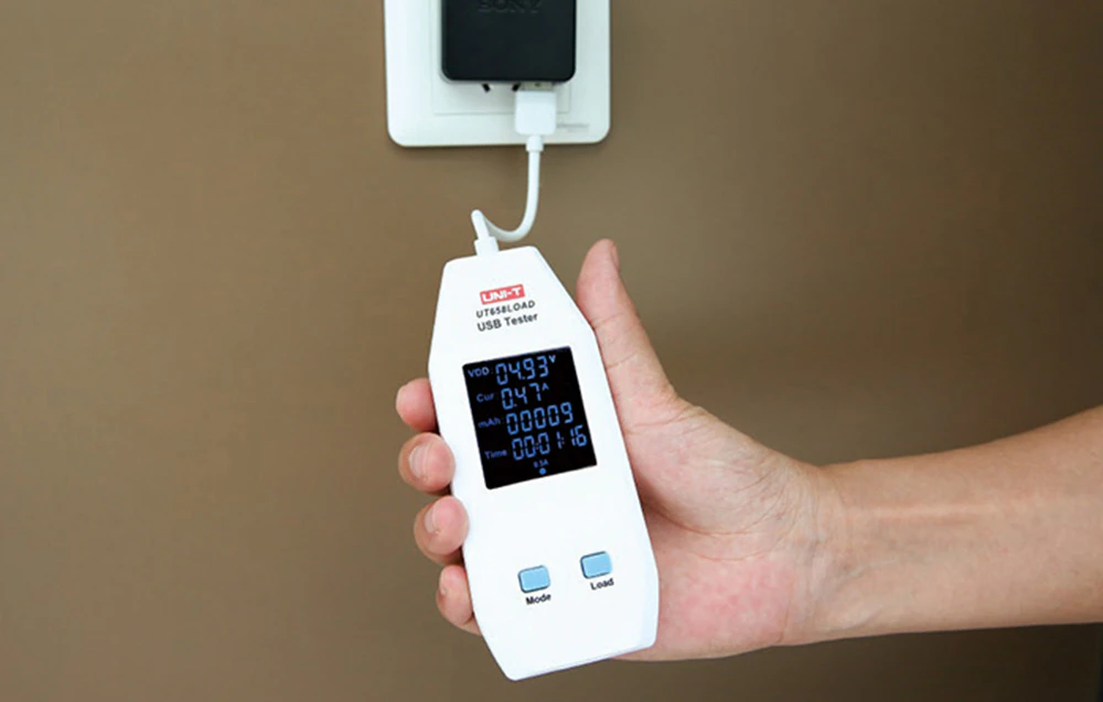 Tester USB conectat la un încărcător de perete, afișând pe ecran parametrii de tensiune și curent de încărcare.