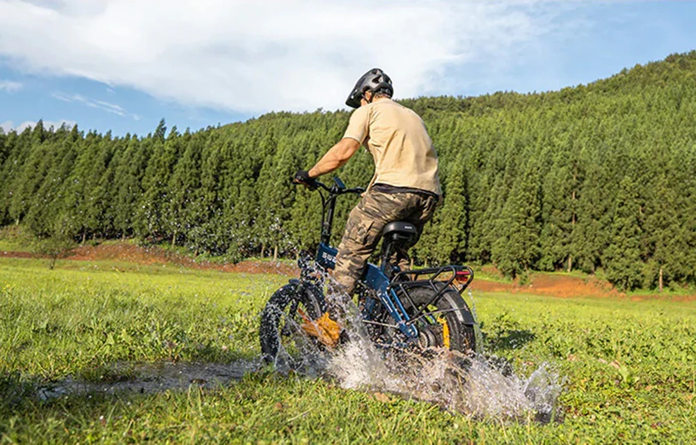 Un bărbat care poartă cască merge cu o bicicletă electrică albastră printr-o băltoacă într-o pajiște