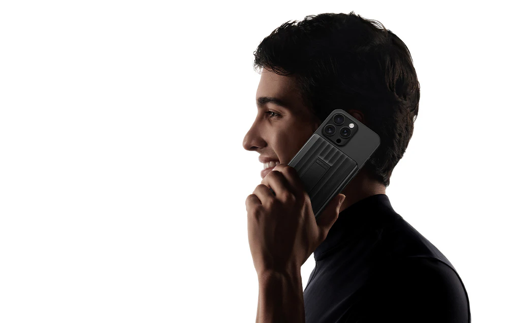Un bărbat cu părul închis la culoare vorbește la telefonul său, care este conectat la un powerbank magnetic.