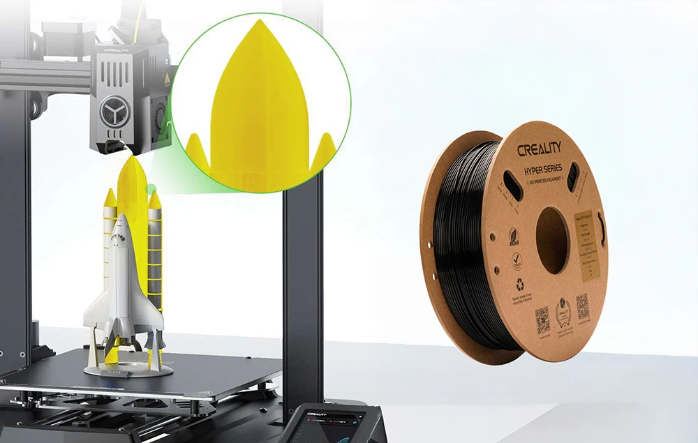 O rachetă galbenă și albă imprimată pe o imprimantă 3D lângă o bobină de filament negru