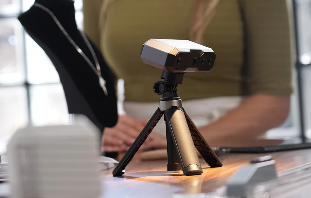 Prim-plan al scanerului 3D de înaltă precizie Revopoint Mini 2 pe un trepied mic, cu un colier pe un suport de expunere negru în fundal