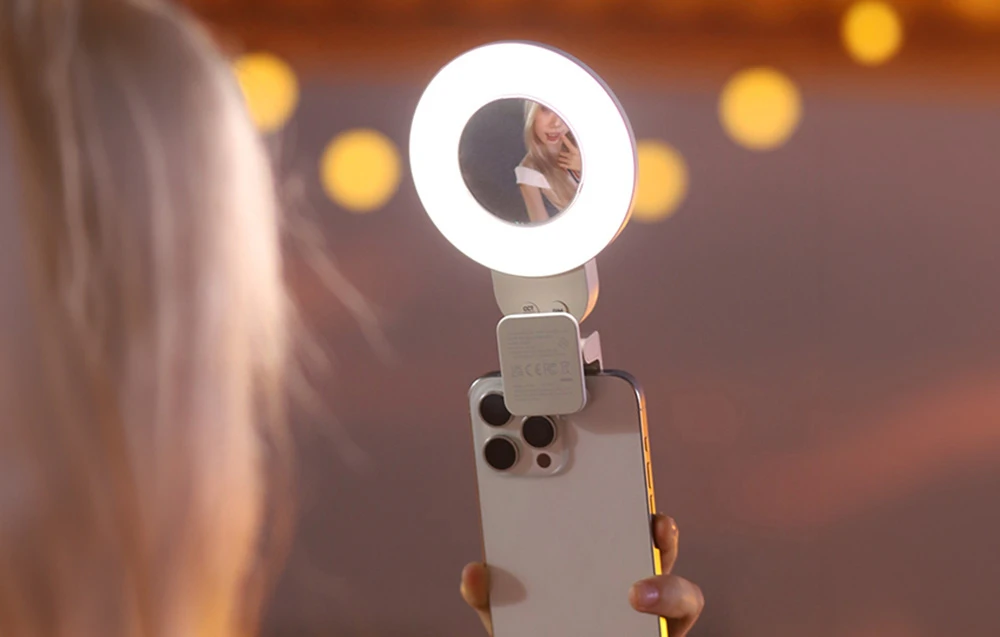Un smartphone cu un inel luminos aprins atașat, prevăzut cu o oglindă care reflectă chipul femeii