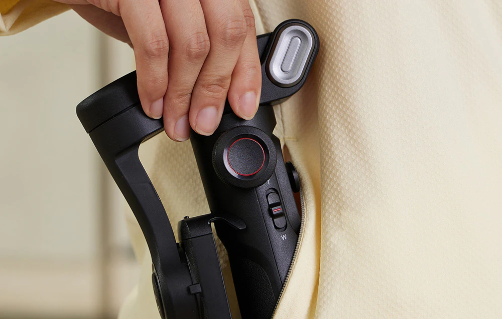 O mână pune un gimbal compact pliabil în buzunarul unui hanorac.