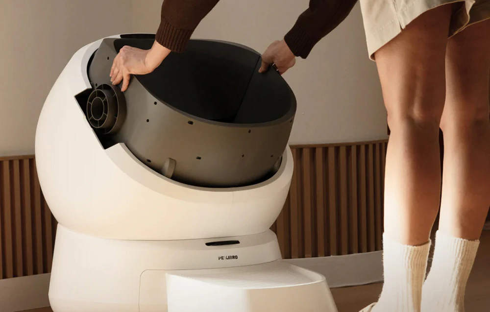O persoană scoate recipientul interior din cutia de nisip automată