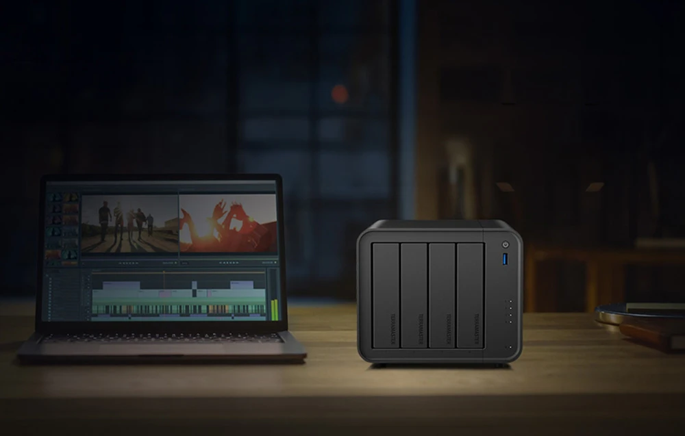 Carcasa NAS cu patru compartimente pentru unități de stocare se află lângă un laptop pe care este deschis un program de editare video