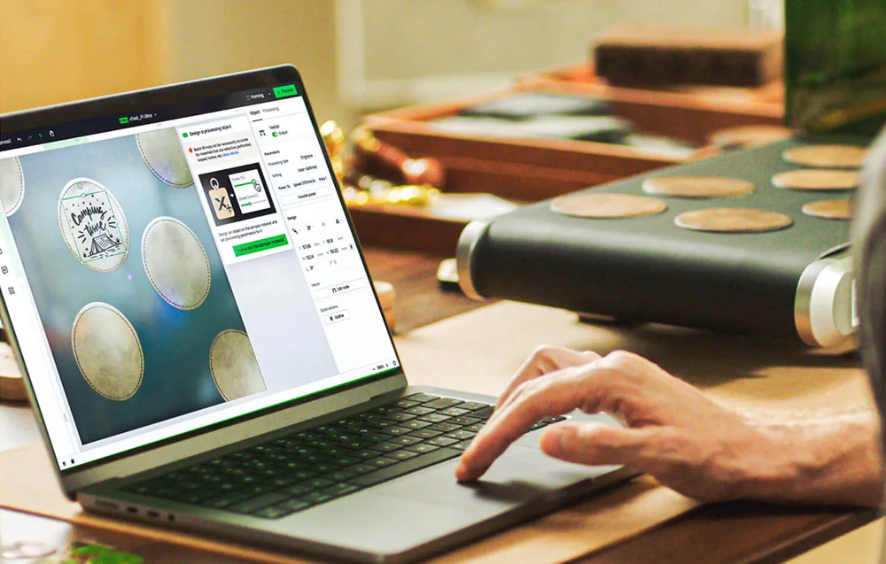 Laptop cu software open-source pentru proiectarea gravurilor pe suporturi rotunde pentru pahare, vizibile în fundal