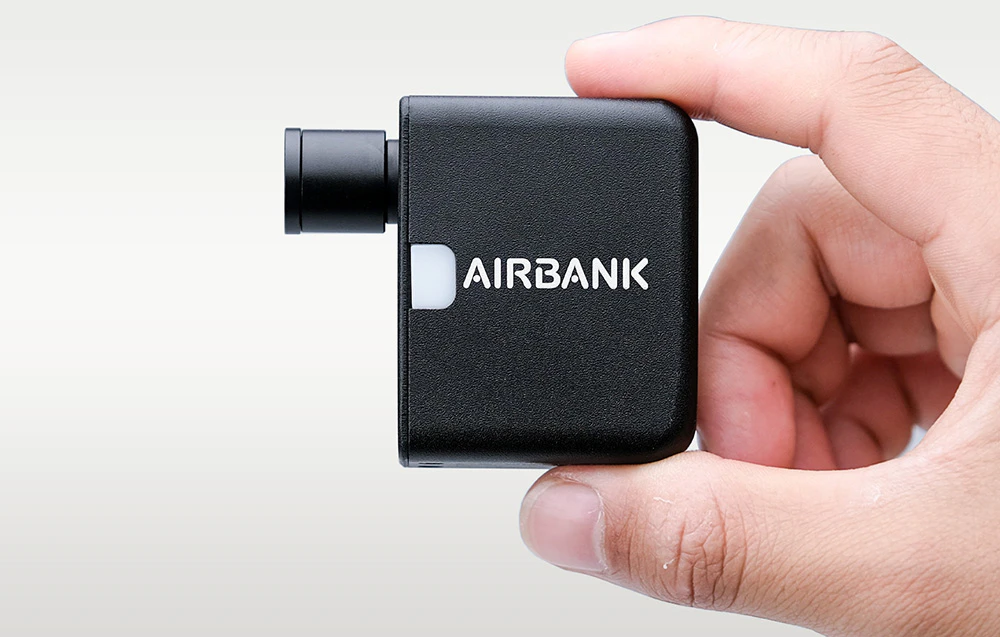 O mini-pompă de bicicletă neagră cu logo-ul Airbank ținută între două degete pe un fundal deschis.