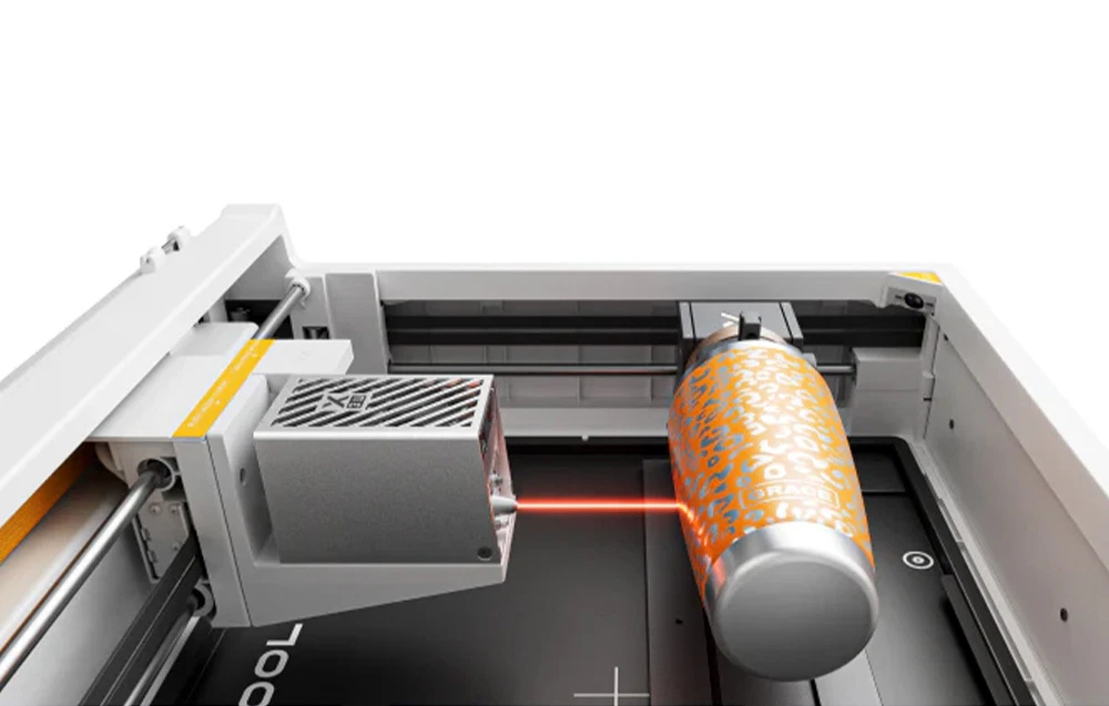 Capul laser xTool gravează o cană termică portocalie montată într-un suport rotativ.