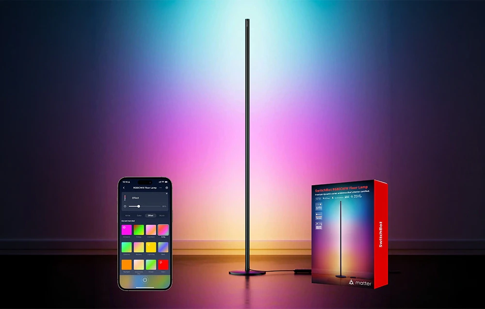 O lampă de podea verticală, în formă de stâlp, care emite lumină multicoloră, așezată lângă un telefon și o cutie.