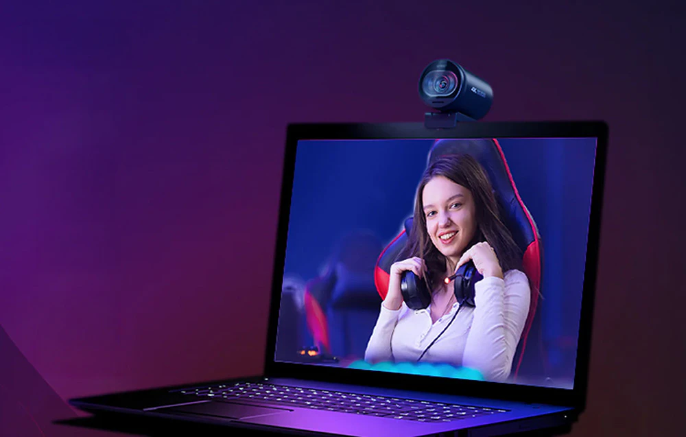 O cameră montată pe un laptop, al cărui ecran arată o femeie zâmbitoare care poartă căști de jocuri.