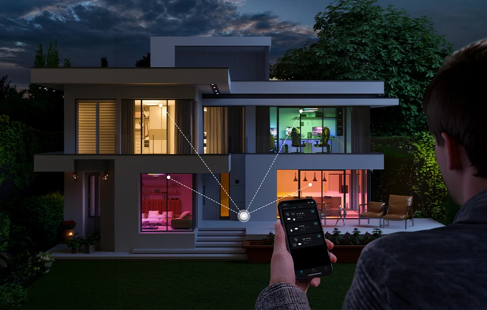 O casă cu două etaje noaptea, cu iluminarea camerelor vizibilă, controlată printr-o aplicație pentru smartphone.