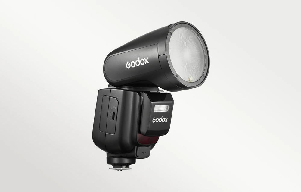Un bliț Godox V1Pro negru cu cap rotund, fotografiat dintr-un unghi pe un fundal deschis