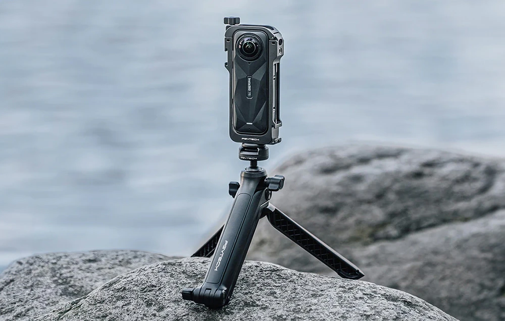 Camera Insta360 X5 în carcasă și pe trepied stă pe o piatră. În fundal se vede apă.