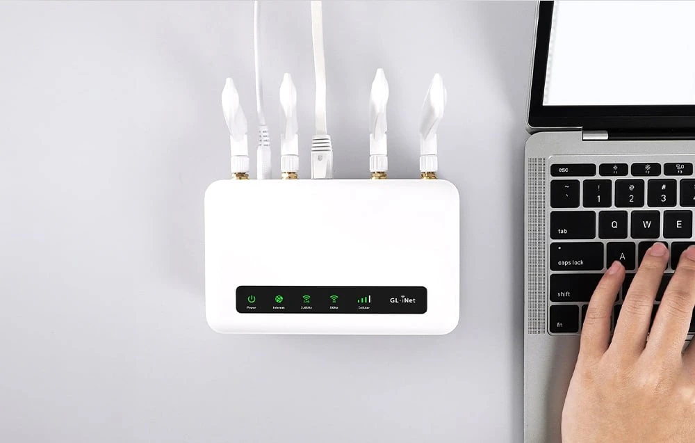 O vedere de sus în jos a unui router alb cu cabluri conectate; lângă acesta se vede o mână care tastează pe tastatura unui laptop.