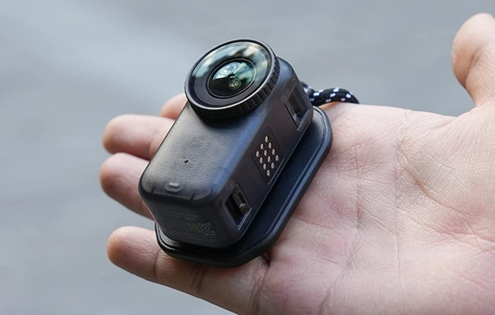 O cameră miniaturală neagră atașată la un suport magnetic, așezată pe o palmă deschisă.