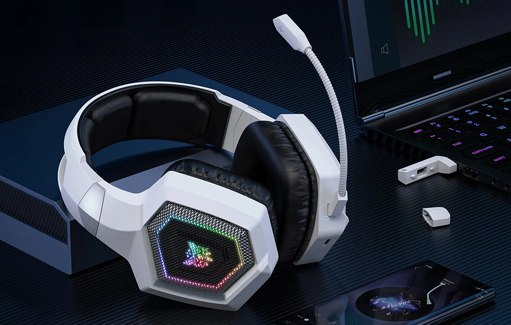 Căști de gaming Onikuma așezate lângă un smartphone și un laptop pe un birou negru