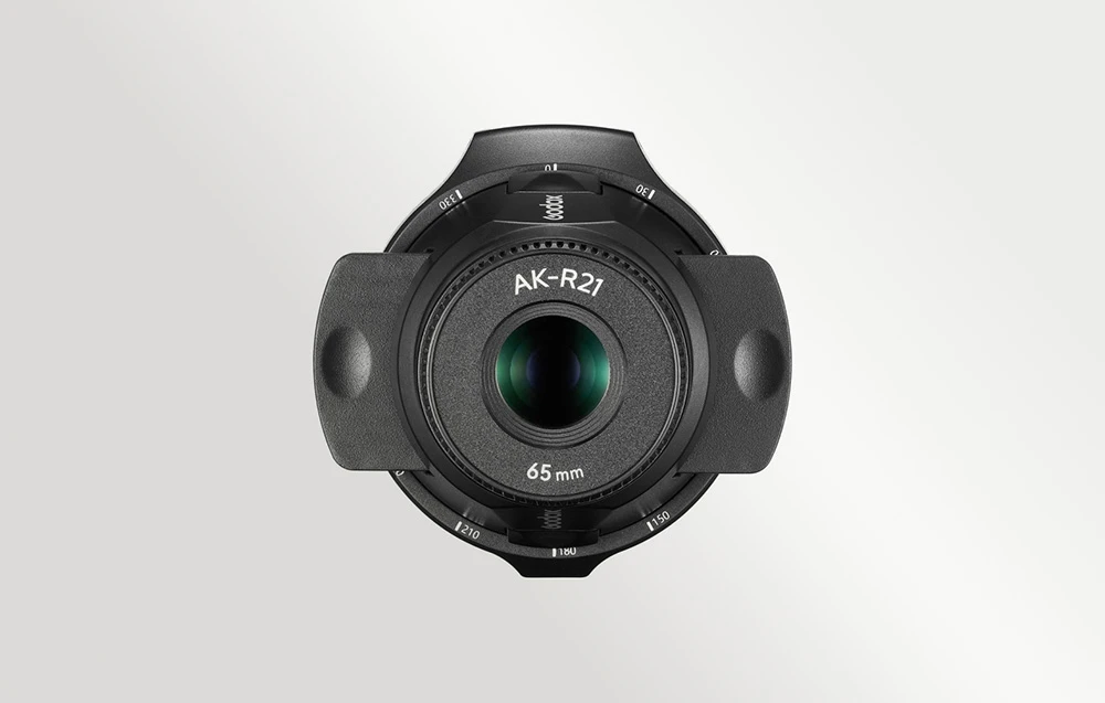 Vedere în prim-plan a accesoriului de proiecție Godox AK-R21 cu obiectiv de 65 mm, din față, pe un fundal gri deschis