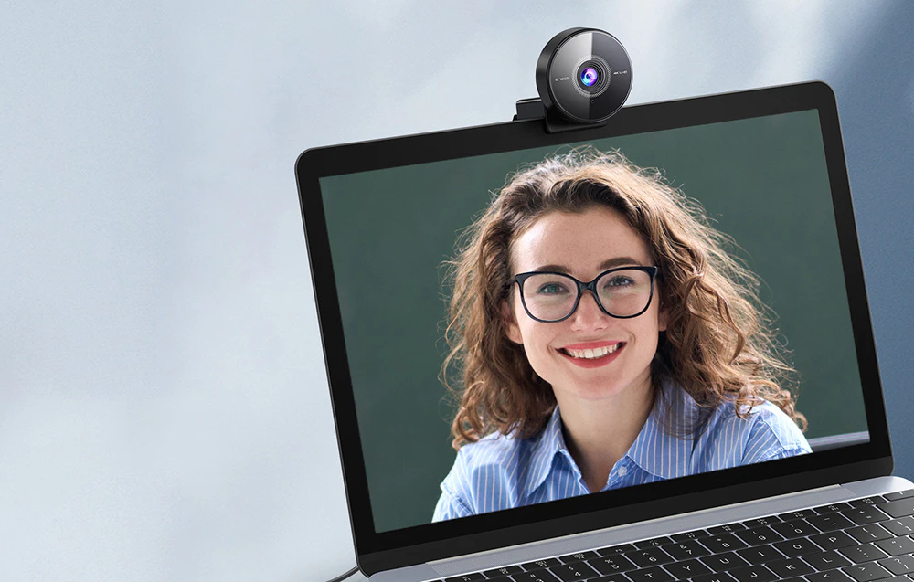 Vedere a unui laptop cu o cameră în partea de sus a ecranului care afișează o femeie zâmbitoare care poartă ochelari.